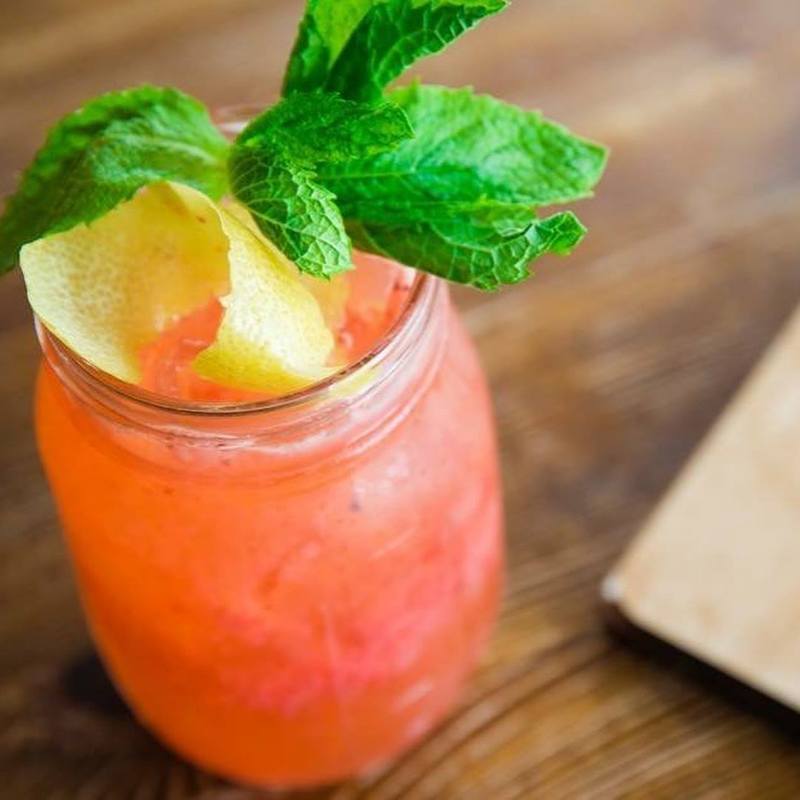 A vivid pink Southside cocktail with fresh mint and a citrus peel.